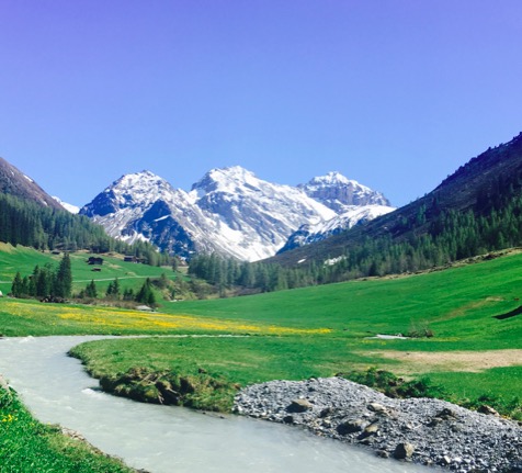 schneebedeckte Berge in der Schweiz, weites Tal mit grünen Wiesen